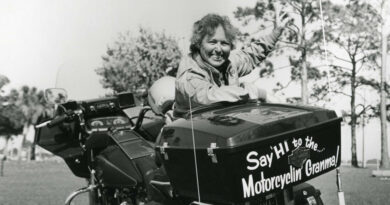 A black and white photo of Hazel Kolb leaning against her motorcycle which has "say hi to the Motorcycling' Granma" on that back of it