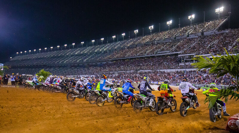 The AMA Supercross riders taking off at the start of the race while the Daytona grandstands rise up in the backdrop